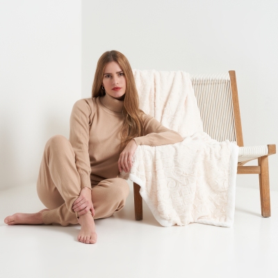 Loungewear shot of a woman in beige knit, seated on a chair. By Nick van der Touw.
