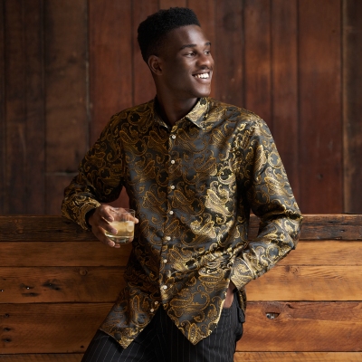 Menswear shot of a man in a gold brocade shirt holding a drink. By Nick van der Touw.