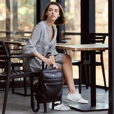 Lifestyle shot of a woman seated at a cafe table with a backpack. By Nick van der Touw.