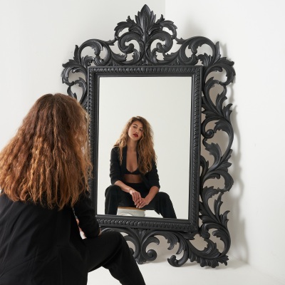 Fashion frame of a woman seated by an ornate mirror in a dark outfit. By Nick van der Touw.