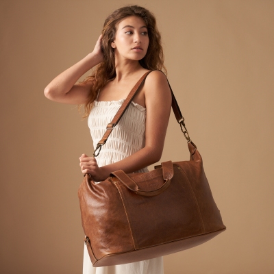 Accessory shot of a tan leather crossbody bag worn by a model. By Nick van der Touw.