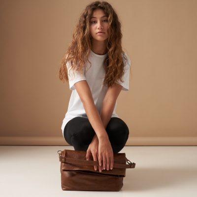 Loungewear shot of a woman in beige knit, seated with a throw. By Nick van der Touw.