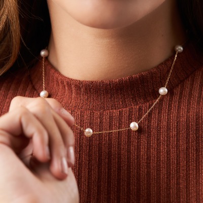 E-commerce shot of a rust knit sweater styled with a pearl necklace. By Nick van der Touw.
