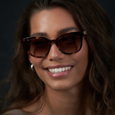 Lifestyle shot of a smiling woman in oversized sunglasses and gold hoops. By Nick van der Touw.