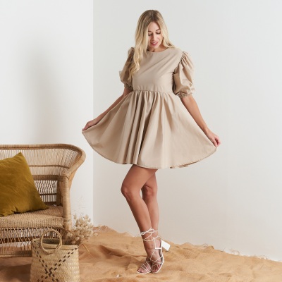 Fashion shot of a woman in a beige dress in a rattan-styled interior. By Nick van der Touw.