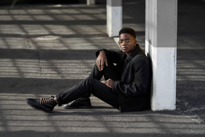 Menswear portrait of a man in all black against an industrial pillar. By Nick van der Touw.