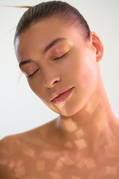 Beauty portrait of Albina with bronzed skin and dappled light patterning. Studio editorial by Nick van der Touw.