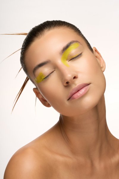 Profile beauty portrait of Albina in yellow eye makeup with a sculptural feather hairpiece. Studio editorial by Nick van der Touw.