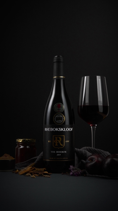 Rhebokskloof wine bottles with a glass of red in dark, moody light. By Nick van der Touw.