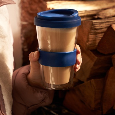 Lifestyle shot of a hand holding a reusable coffee cup with a blue band. By Nick van der Touw.