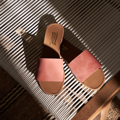 Product shot of pink suede slide sandals on a striped rug. By Nick van der Touw.