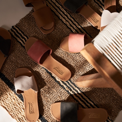 Product shot of tan leather slide sandals on a woven rug. By Nick van der Touw.