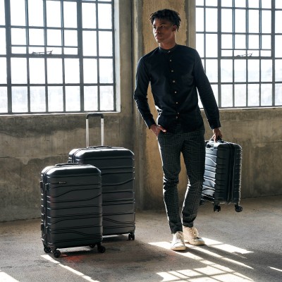 Travel shot of a man with a black wheeled suitcase. By Nick van der Touw.