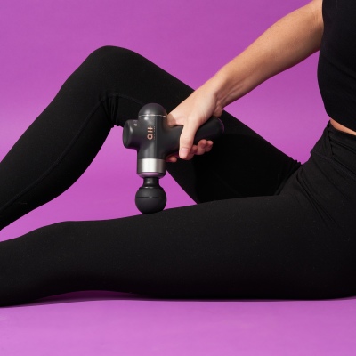 Product shot of a handheld massage gun against purple. By Nick van der Touw.