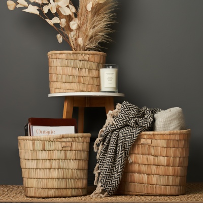 Homeware display of woven baskets, a candle and a throw. By Nick van der Touw.